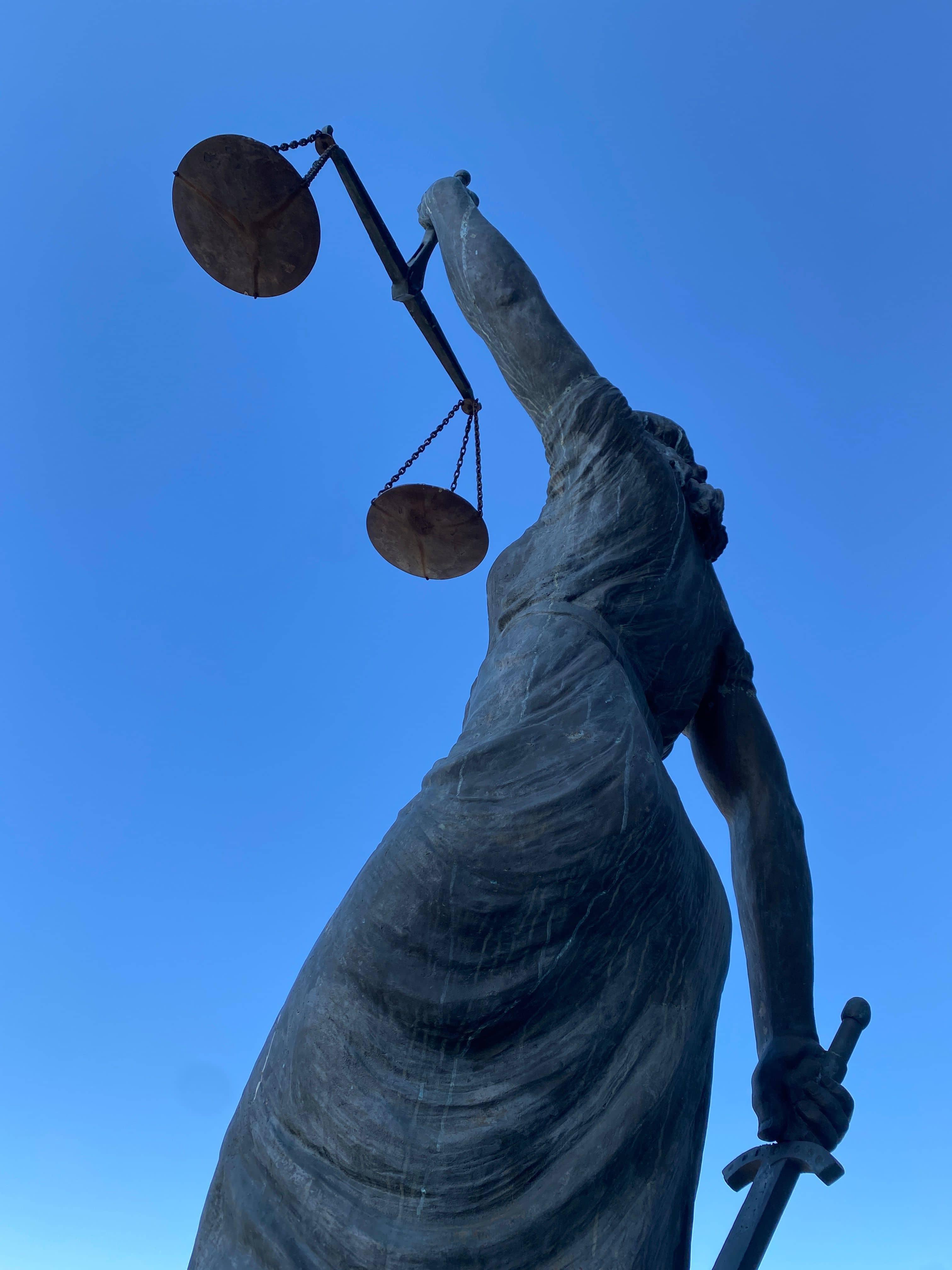 Bronzene Justitia mit Waage und Schwert vor blauem Himmel